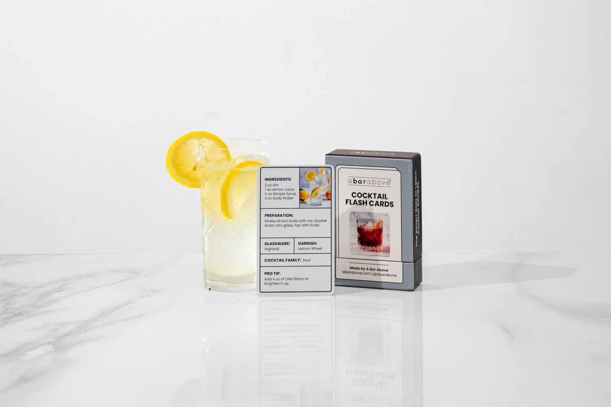 a refreshing cocktail in a tall glass, next to cocktail recipe cards in a gift box