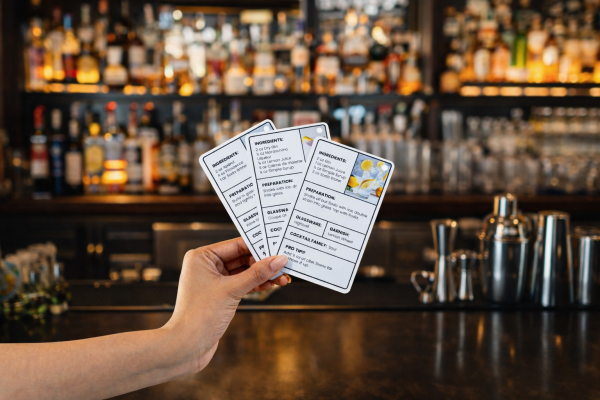a hand holding cocktail recipe cards in a bar